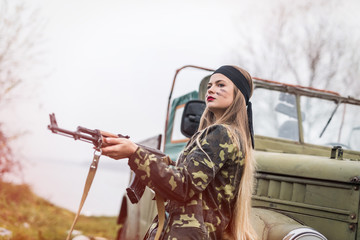 Woman soldier with rifle posing near military car