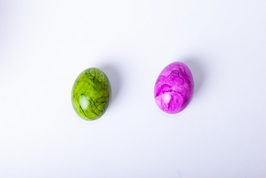 Two painted easter eggs (green and purple) laying on white background