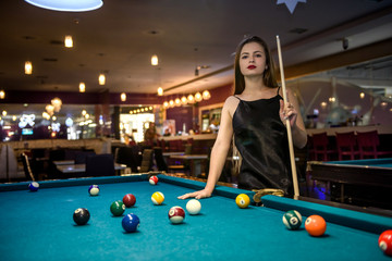 Beautiful woman in black dress posing with billiard cue