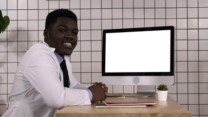 Black doctor talking to camera sitting next to computer screen. White Display.