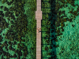 Couple homme femme allongé sur Ponton en bois eau turquoise drone aérienne