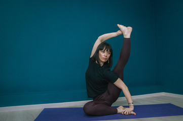 A girl with dark hair practices yoga in a hall with turquoise walls.