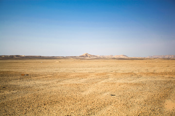 Deserted desert and complete peace of mind. Motionless stones and silence. Desert with hillmamite in the distance and blue sky - obrazy, fototapety, plakaty