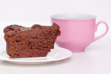 Delicious chocolate cake on plate with pink cup of coffee on table on light background