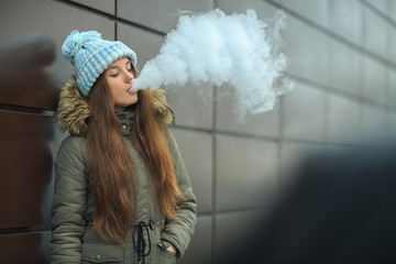 Vape teenager. Young pretty white girl in blue cap is smoking an electronic cigarette opposite...