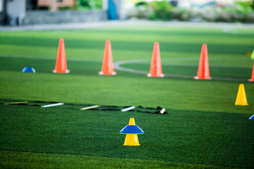 Fototapeta na wymiar Cone markers is soccer training equipment on green artificial turf with blurry kid players training background