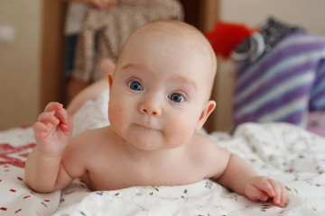 Beautiful five-month blue-eyed toddler baby girl lying on her stomach, various emotions on her face. Infant look. Maternal care. Chil care. Close-up.