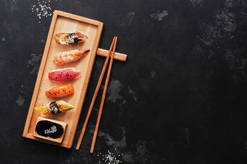 Assorted sushi set on a wooden plate, dark stone background. Japanese food sushi, soy sauce, chopsticks. Top view, copy space.