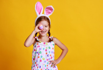 funny happy child girl with easter eggs and bunny ears on yellow