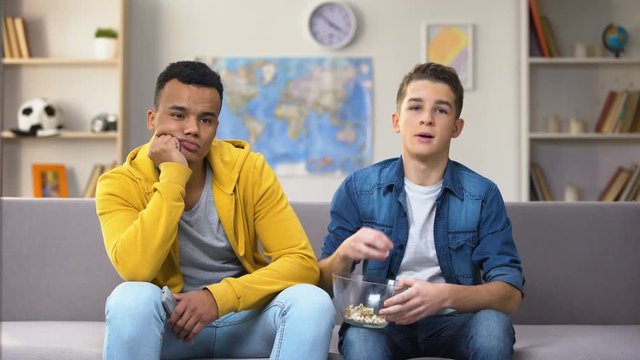 Bored multiracial boys watching TV eating snacks, slow old technology connection
