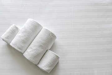 White towels set roll up on the white bed in modern hotel bedroom with copy space