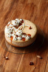 Almond Cheesecake decorated with whipped cream and salted caramel, on round transparent cake stand, on wooden table.