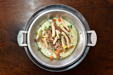 The famous breakfast thai food Panned eggs is fried egg topping with sausage, vegetable and bacon in the hot pan.