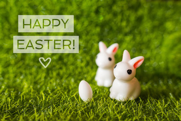 two figures of a rabbit and an egg on the grass.