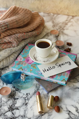 white coffee Cup with the text Hello Spring and a warm sweater on a marble table.