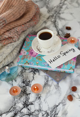 white coffee Cup with the text Hello Spring and a warm sweater on a marble table.