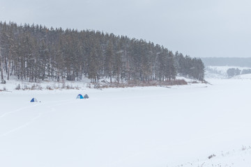 Scenic picture-postcard landscape with lake, forest and mountains. Beautiful view in winter. Tents of fishermen on the ice.