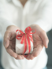 hand holding white gift box with red ribbon