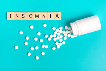 White bottle and pills on a blue background. The concept of medicine, problems and treatment of insomnia. Flat lay. Top view. Copy space.