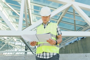 Fototapeta premium Portrait of male engineer at construction site, builder looks at blueprint. Building, development, teamwork and people concept