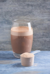 Scoop of Whey Protein and a Glass of Chocolate Protein Shake with milk and banana. Sport nutrition. Wooden background. Copy space. 