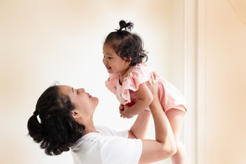 Mother raising her daughter up in the air,with smile and happy face,Mother-child bond,blurry light around