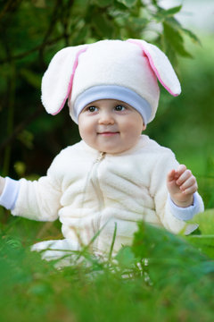 Little chubby girl in bunny costume seating on grass.