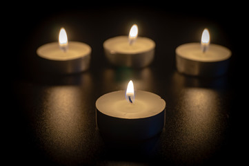 Obraz na płótnie Canvas Four tea candles with reflection on black
