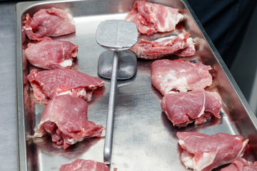 Fresh meat pork tenderloin in restaurants kitchen on metal tray and hammer, ready for roasting in oven. Concept cooking semi-finished product, roasting, roasted, grilled meat