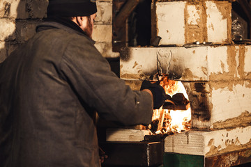 Bearded blacksmith throws coal into the furnace.