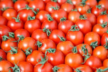 Closeup plenty red fresh ripe cherry tomatoes together with stems are awaiting distribution in box on farmers market. Concept of selling vegetables in supermarket, grocery store