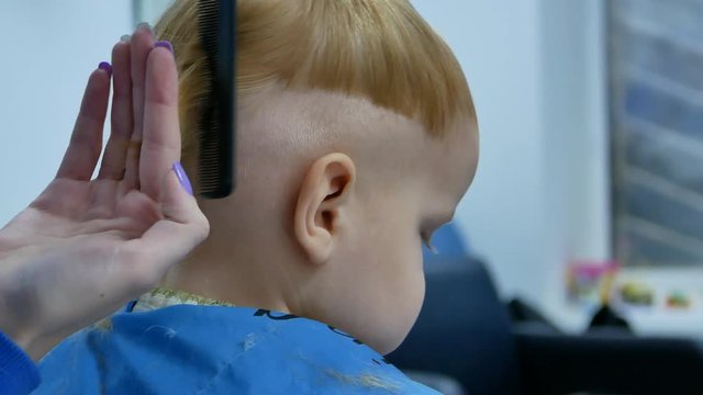 barber trying to make haircut with shears while little boy turn spin his head, view from the back 4k closeup video footage
