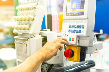 Operator or tailor working on control panel of modern and automatic high technology sewing or embroidery machine for textile - clothing apparel making manufacturing process in industrial