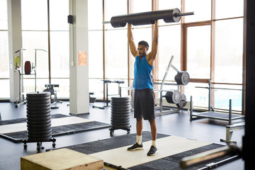 Fototapeta premium Young sportsman in activewear lifting heavy barbell over his head while exercising in cross training center