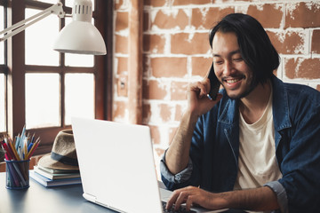 Young Asian man talking on phone and working on laptop for business creative designer