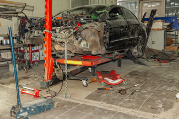 A broken car with a violation of geometry is on the stocks for leveling and repair in the workshop and auto service for the restoration of vehicles on building berth with chain and red hook