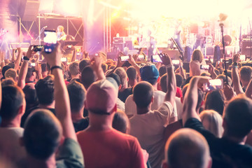 people standing with arms raised shoot a video on the phone at a street music show, blurred background