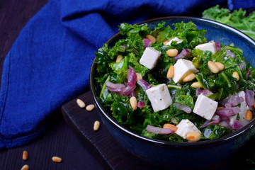 Salad with kale, red onion, feta cheese and pine nuts in the blue bowl