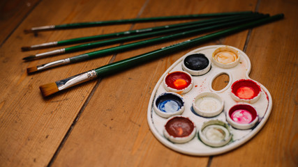 white curly palette with watercolors next to green brushes everything is placed on a wooden background