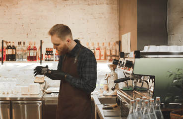 Portrait of the husband of the owner of the cafe is with the holder in the hands of a professional coffee machine. Professional barista in a cafe in the workplace holds a holder in his hands.