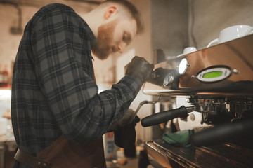 Portrait of a barista's husband steaming milk for cappuccino on a professional coffee machine. Concentrated barista owner prepares coffee in the coffee shop.