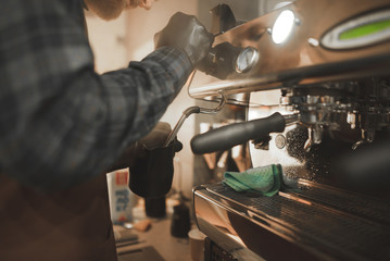 Close -up photo, barista steaming milk in pitcher on a professional coffee machine. Barista professional cooks coffee in the coffee shop. Man makes a cappuccino on a professional coffee machine.