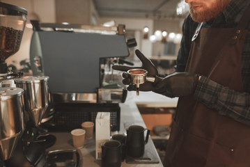 Fototapeta na wymiar Barista holding a holder with ground coffee and ready for preparing coffee for a professional coffee machine. Bartender prepares coffee, holding a portafilter in hands. Coffee concept