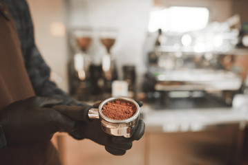 Barista holds in his hands a holder with fresh ground coffee, close up. Cooking coffee in the coffee shop. Coffee culture concept. Background