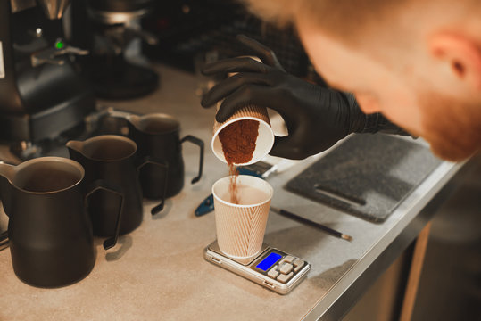 Close up photo of barista weighing coffee grains on digital scale. Hand of male barista pouring roasted coffee grains in a paper cup and weighing it before brewing coffee.
