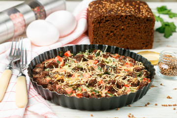 Breakfast in a rustic style. Homemade bread casserole strata with cheese, egg, ham, parsley. Black rye bread with coriander. Selective focus