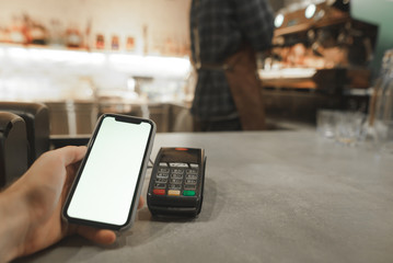 Mobile payment in cafe with smartphone nfc near field communication wireless technology. Paying with smartphone at the coffee shop, while male barista is preparing coffee at the coffee machine.