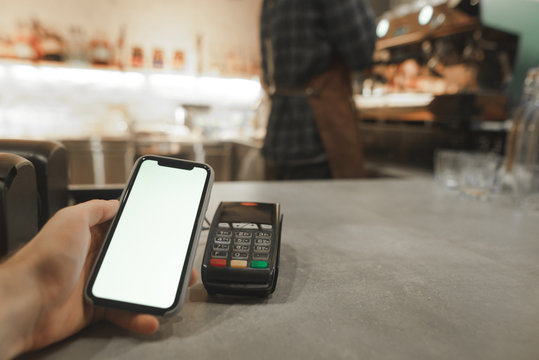 Mobile payment in cafe with smartphone nfc near field communication wireless technology. Paying with smartphone at the coffee shop, while male barista is preparing coffee at the coffee machine.