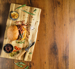 Homemade beef burger with crispy bacon and vegetables on rustic serving board