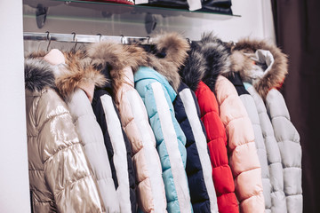 Shelving in a clothing store. Women's down jackets with natural fur hanging on a hanger.